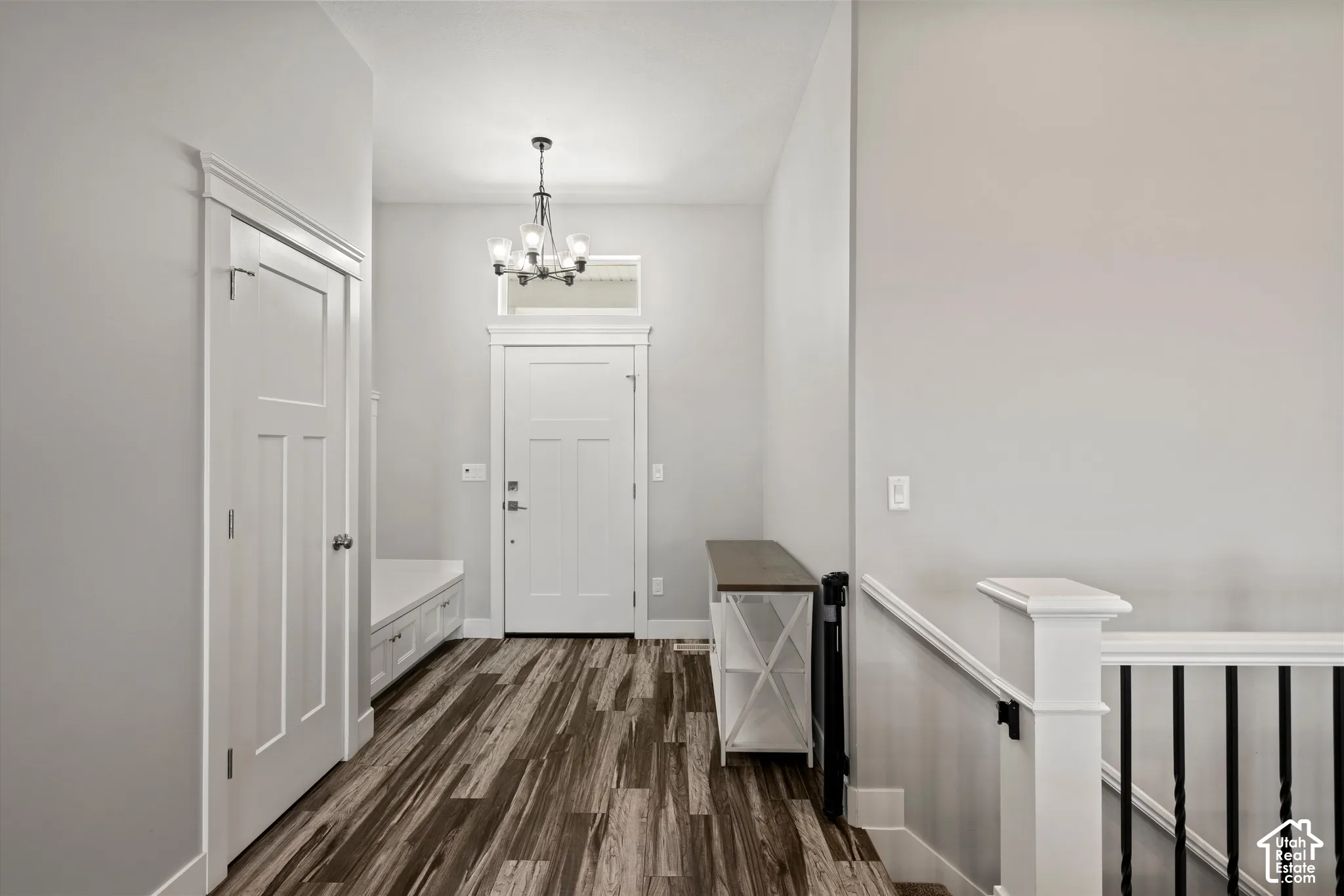 Entryway featuring wood-finish flooring, a built-in bench with storage, a five-light chandelier, a transom window, and a staircase with white newel posts and black iron balusters