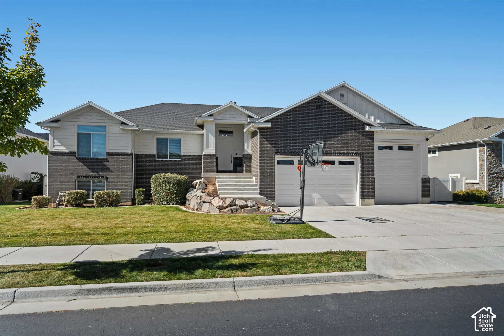 Two-story residence featuring a brick and siding exterior, multi-car garage, concrete driveway, and front lawn with mature landscaping