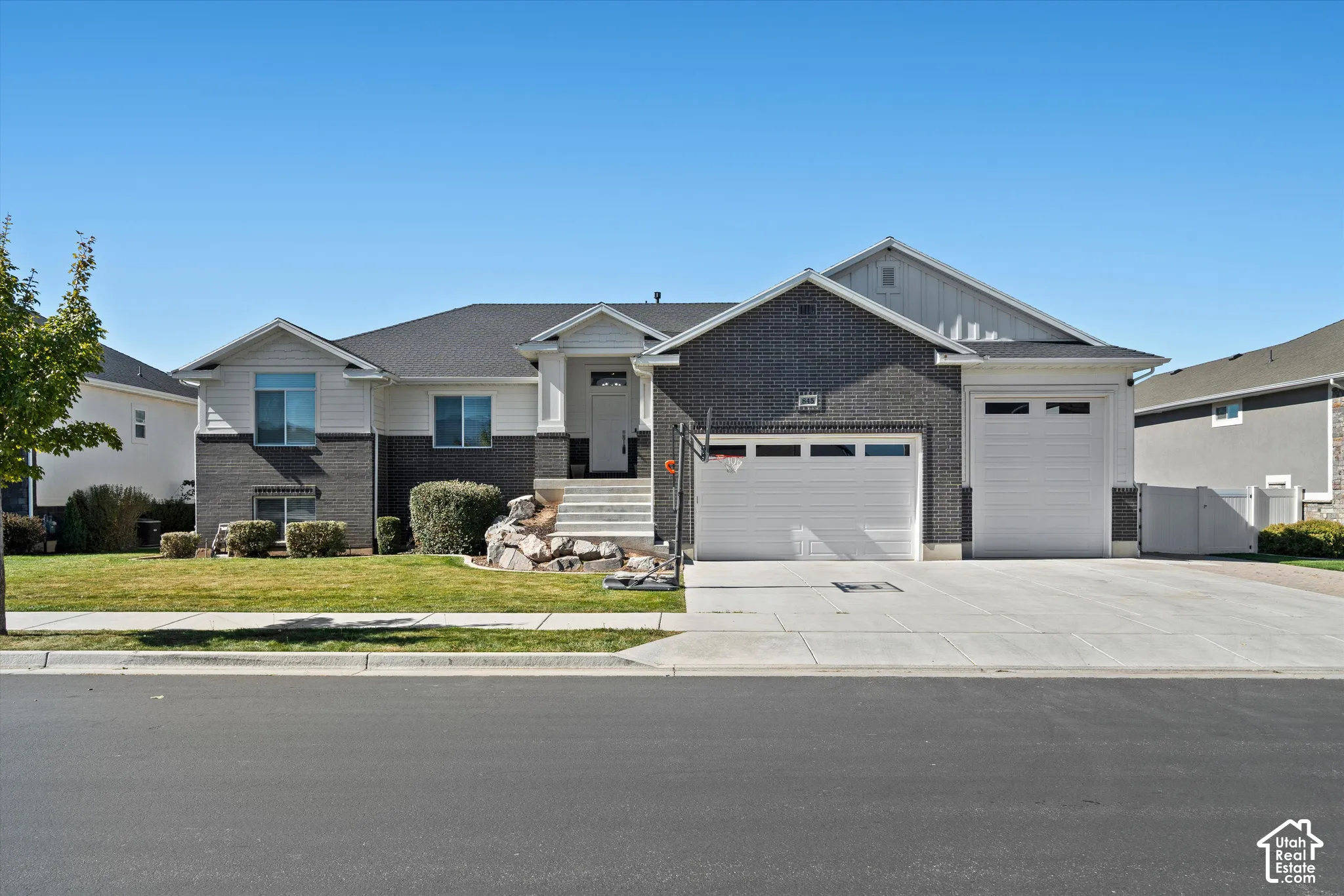 Split-level residence featuring a gray brick and white siding exterior, an attached two-car garage, an additional single-car garage, a concrete driveway, and a manicured lawn