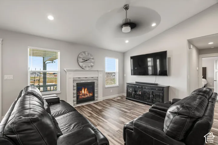 Vaulted ceiling with a ceiling fan, recessed lighting, wood-finish flooring, and a fireplace with a white mantel and tile surround