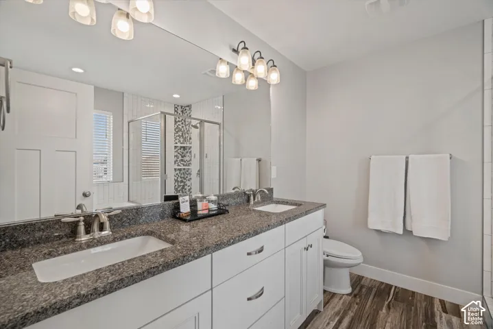 Dual vanity with dark stone countertop, white cabinetry, wood-finish flooring, and a glass-enclosed shower featuring mosaic tile accents