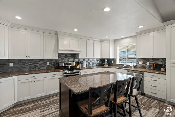 Kitchen featuring white cabinetry, stone countertops, a tile backsplash, wood-finish flooring, and recessed lighting