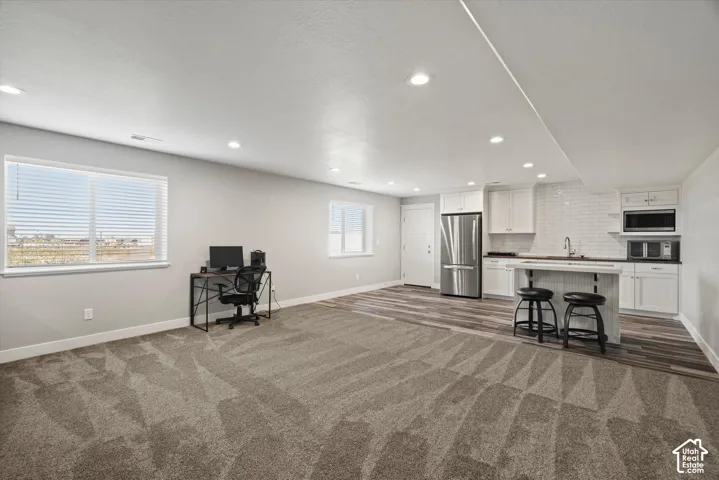 Recessed lighting throughout, two windows with blinds, wood-finish flooring, white subway tile backsplash, and stainless steel refrigerator