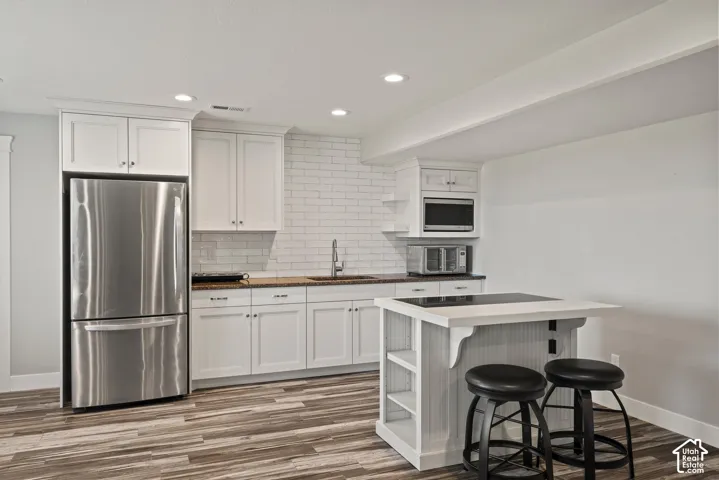 Full kitchen featuring white cabinetry, stainless steel refrigerator, white subway tile backsplash, and wood-finish flooring