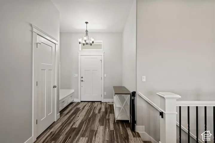 Entryway featuring wood-finish flooring, a built-in bench with storage, a five-light chandelier, a transom window, and a staircase with white newel posts and black iron balusters