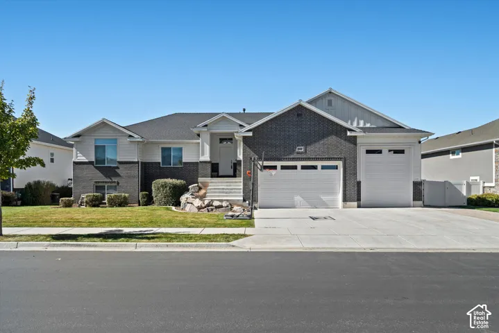 Split-level residence featuring a gray brick and white siding exterior, an attached two-car garage, an additional single-car garage, a concrete driveway, and a manicured lawn