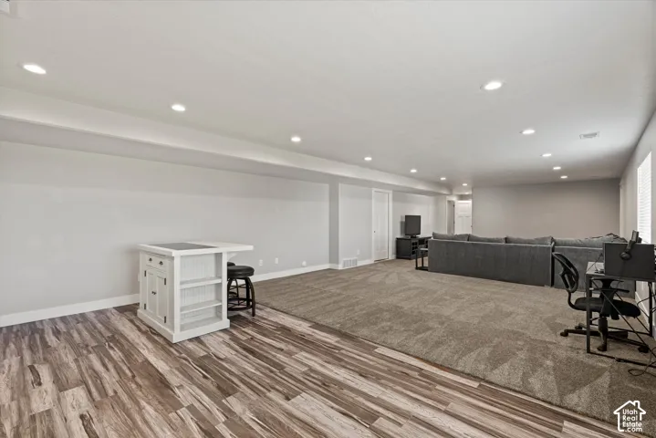 Recessed lighting illuminates this expansive room featuring wood-finish flooring and plush carpeting