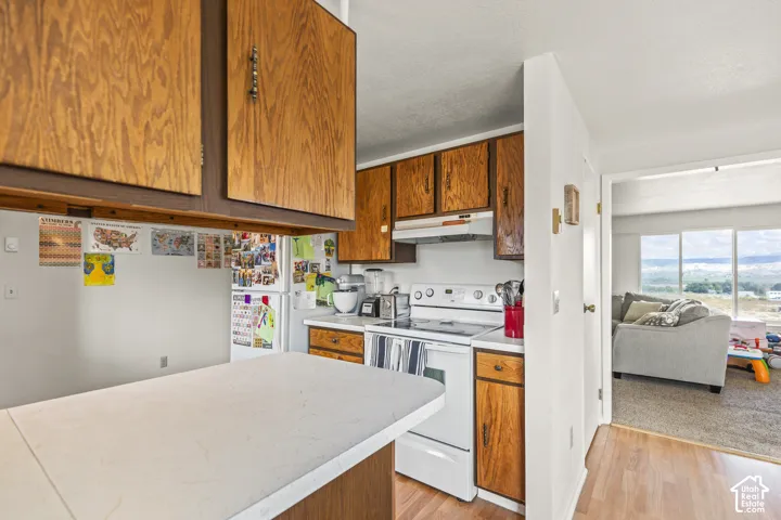 Kitchen with wood cabinetry, white countertops, and white appliances