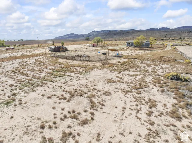 Expansive open land with distant mountains, a residential structure, and an animal enclosure with a partial shade structure