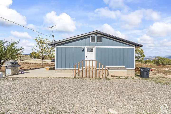 Exterior siding in a blue finish, white trim, white exterior door, and a gravel foreground