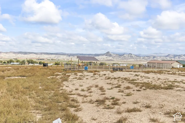 Expansive open land with distant mountain ranges, a metal-roofed shelter, and a fenced enclosure