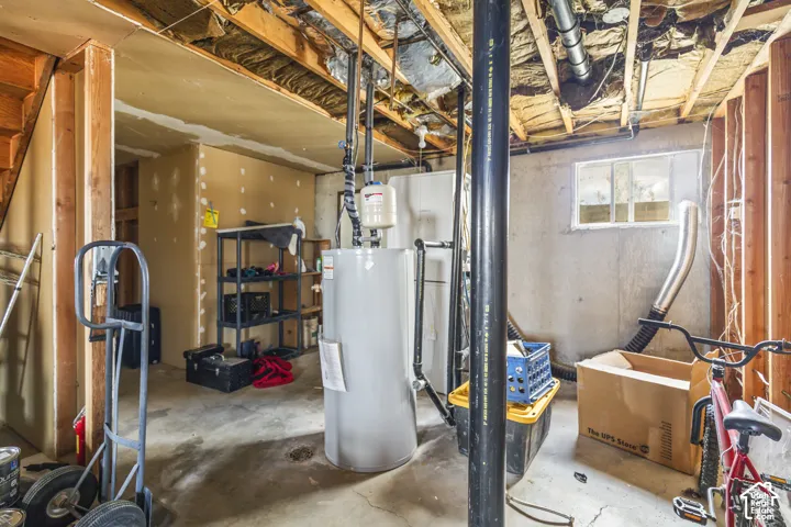 Unfinished basement space featuring a water heater, exposed wood framing, and a small transom window