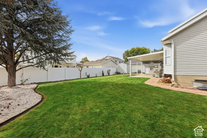 Expansive lawn with a mature tree, white privacy fencing, and a covered patio area