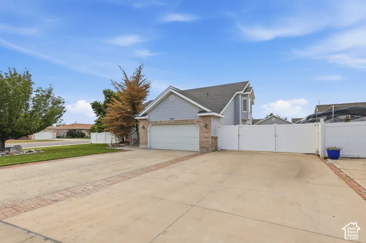 Two-car garage with white door, brick accents, concrete driveway with brick detailing, and white privacy fencing