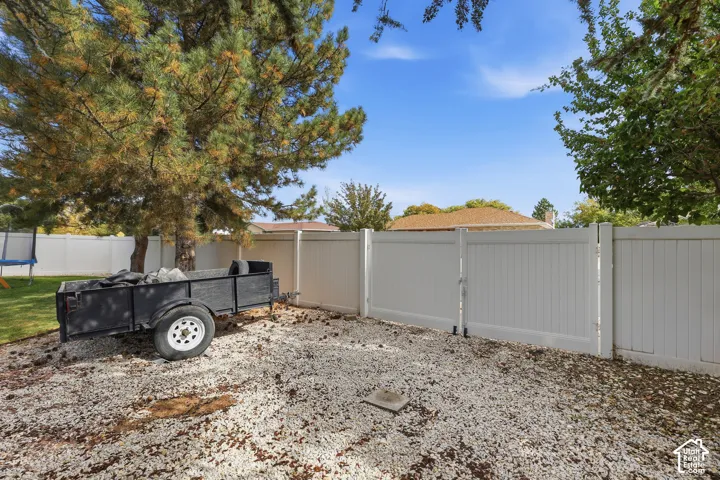 Backyard area featuring a gravel surface, a white privacy fence with a gate, and mature trees