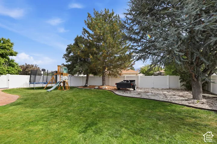 Expansive backyard featuring a lush lawn, white vinyl fencing, and mature trees providing natural shade