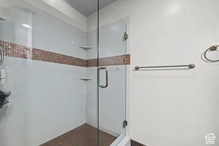 Enclosed shower with clear glass door, mosaic tile accent band, and integrated corner shelving