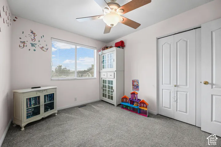 Carpeted room featuring a ceiling fan with integrated lighting, a window with horizontal blinds, and a built-in closet with double doors