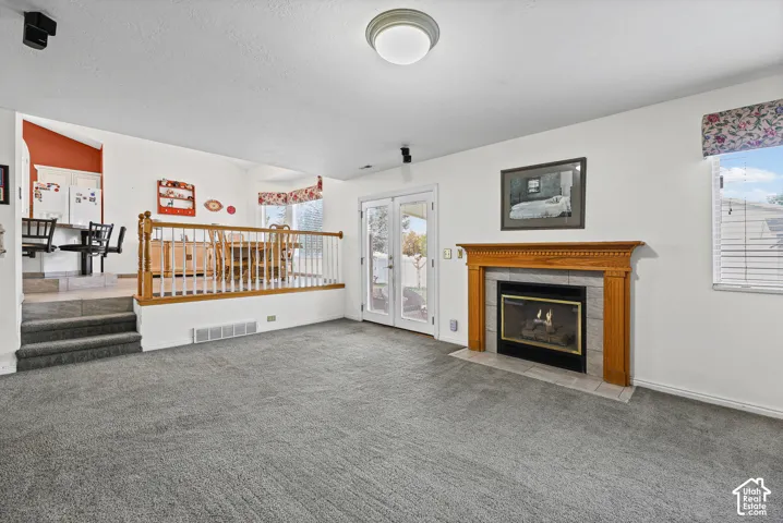 Carpeted living area featuring a fireplace with a wood mantel and tile surround, French doors, and a raised dining area with wood railing