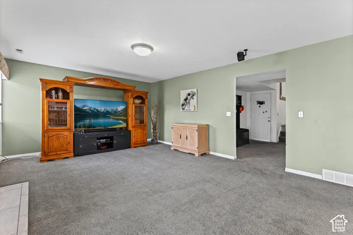 Recessed lighting, light-colored walls, gray carpeting, and a built-in entertainment center