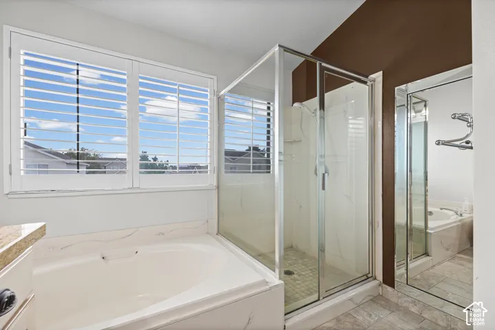 Spacious bathroom featuring a built-in soaking tub, a glass-enclosed shower, and a window with plantation shutters