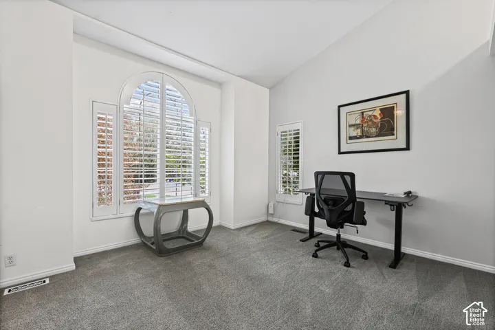 Vaulted ceiling, arched window with plantation shutters, additional window with plantation shutters, and grey carpet flooring