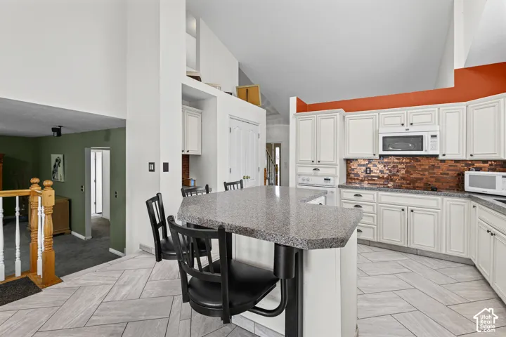 White cabinetry with dark hardware, a copper-toned tile backsplash, and light-toned countertop