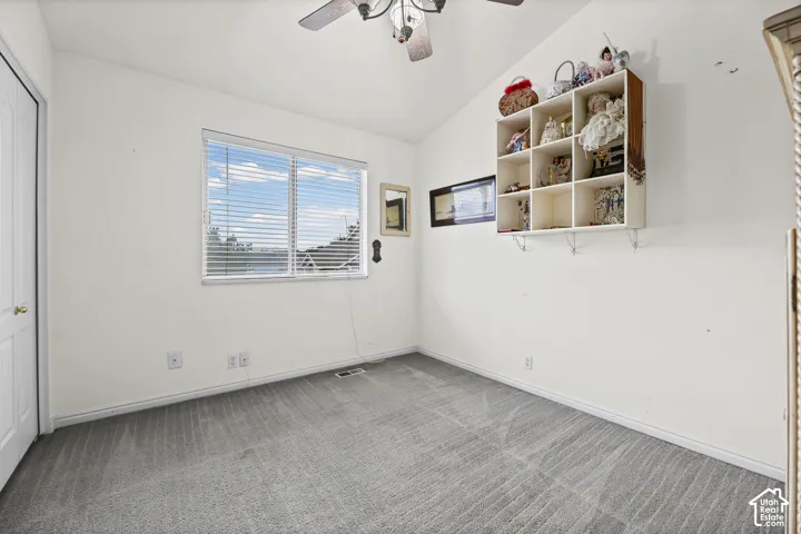 Vaulted ceiling, ceiling fan with light fixture, double-pane window with blinds, light gray carpet, and white trim
