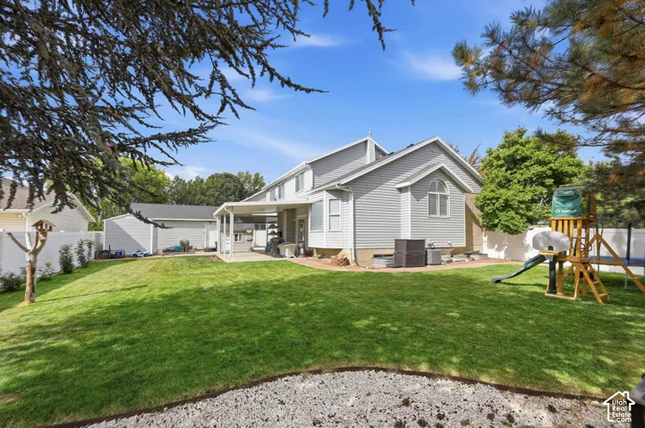 Expansive backyard featuring a manicured lawn, established landscaping, and a covered patio
