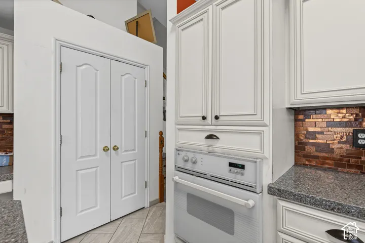 White paneled cabinetry with dark hardware, integrated wall oven, patterned tile backsplash, and speckled countertops