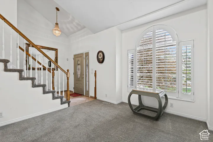 Vaulted ceiling with an elegant chandelier, wood-finish staircase with white balusters, and an arched window with plantation shutters