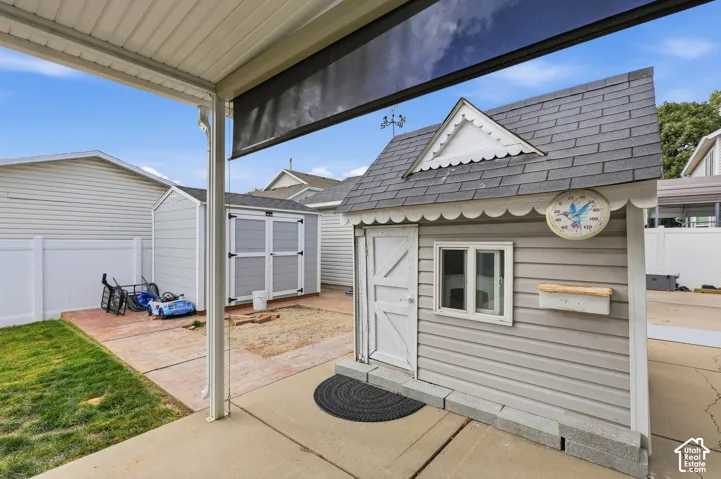 Covered patio area with a concrete surface, adjacent to a structured shed and a fenced property line