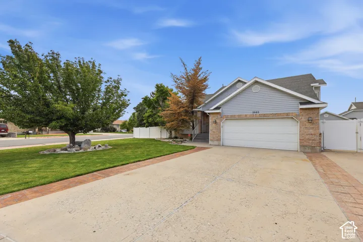 Brick and siding exterior featuring a multi-car driveway with accent paving, a manicured lawn, and a privacy fence