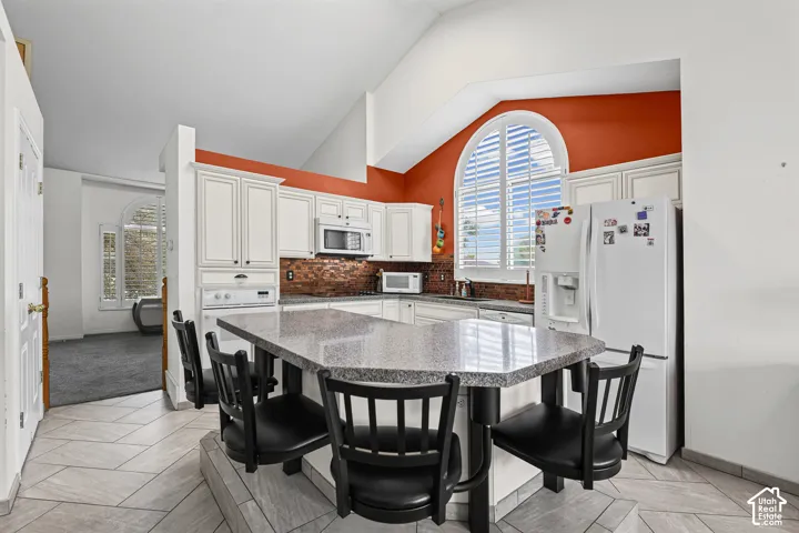 Vaulted ceiling kitchen featuring white cabinetry, a large kitchen island with counter seating, a tiled backsplash, and an arched window