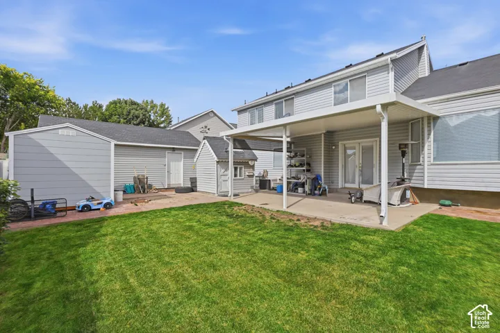 Expansive backyard featuring a manicured lawn, a large covered patio, and a separate storage shed