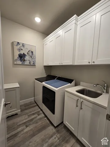 White shaker cabinetry, wood-finish flooring, recessed lighting, stainless steel utility sink, and a light-toned countertop