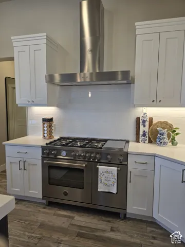Stainless steel professional-grade range with a matching range hood, white shaker-style cabinetry, light-toned countertops, white subway tile backsplash, and wood-finish flooring