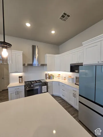 Kitchen featuring white cabinetry, a stainless steel range with a coordinating hood, light-toned countertops, and wood-finish flooring