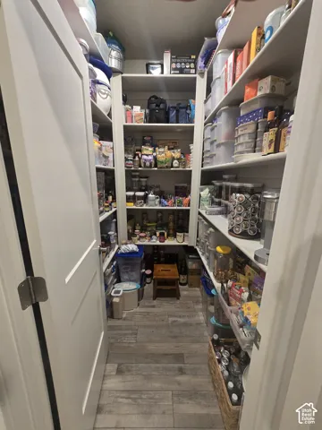 Walk-in pantry with extensive shelving, dual panel doors, and wood-finish flooring