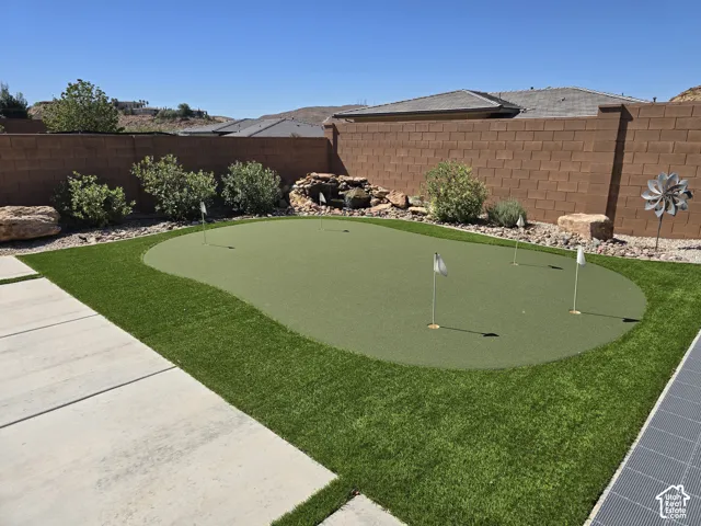 Private backyard featuring a putting green, artificial turf, concrete patio, and a rock wall with integrated water feature