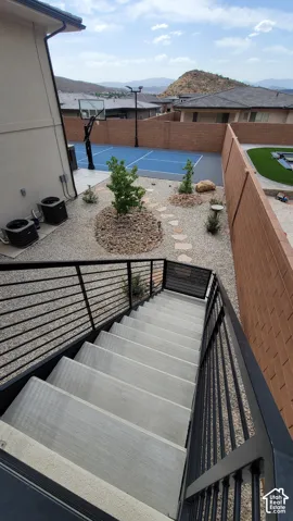 Terraced outdoor space featuring a private sports court, xeriscape landscaping with mature plantings, and a modern staircase with horizontal metal railings