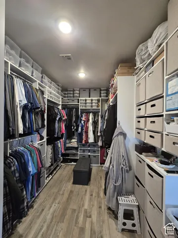 Custom closet organization system with extensive built-in shelving, multiple hanging rods, and wood-finish flooring