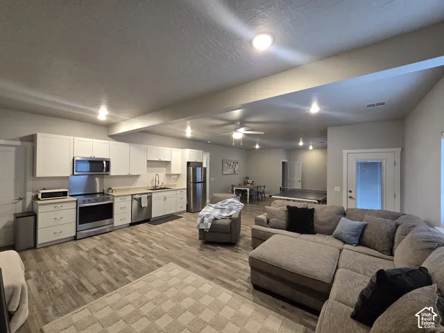 Open-concept lower level featuring a full kitchen with stainless steel appliances and white cabinetry, wood-finish flooring, recessed lighting, and a ceiling fan