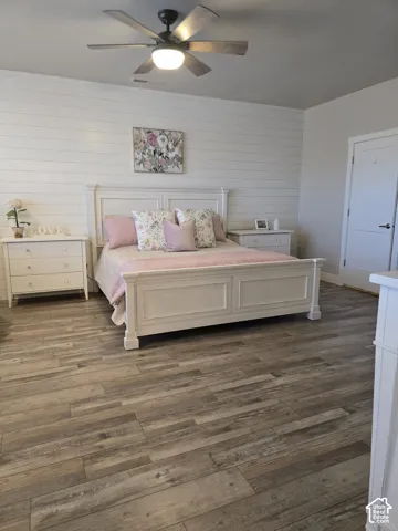 Wood-finish flooring, shiplap accent wall, white paneled door, and ceiling fan with integrated lighting