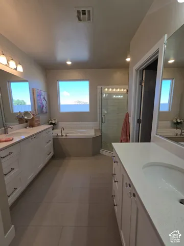 Dual vanities with white cabinetry, a built-in soaking tub, and a separate glass-enclosed shower