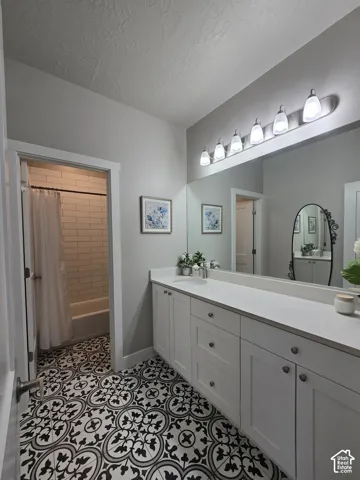 Black and white patterned tile flooring, an elongated vanity with a single sink, white cabinetry with silver hardware, a large mirror, and a built-in bathtub with subway tile surround