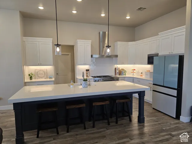 Kitchen featuring a large central island with a white countertop, white shaker-style cabinetry, stainless steel range with matching hood, integrated appliances, and wood-finish flooring