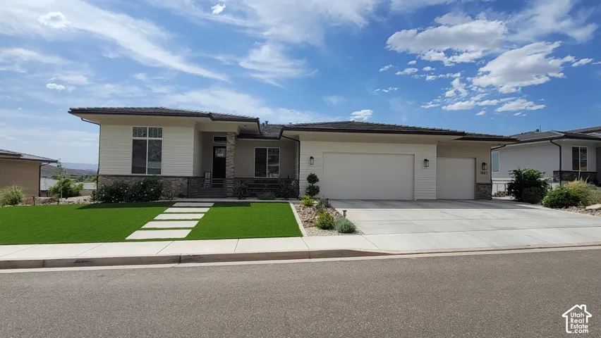 Contemporary exterior design with stone and siding accents, a multi-pane front window, a two-car garage with overhead lighting, a concrete driveway, and a manicured artificial turf lawn