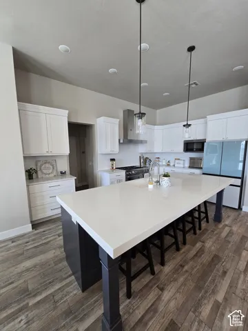 Spacious kitchen featuring an expansive central island with a light-colored countertop, white upper and lower cabinetry, stainless steel range hood, and wood-finish flooring