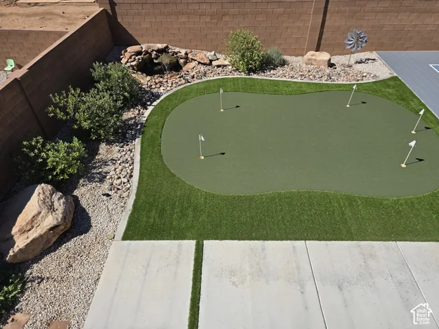 Backyard putting green, artificial turf, decorative rock landscaping, water feature, and paved patio